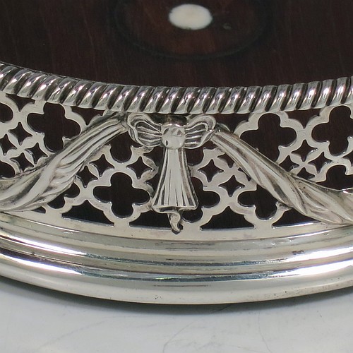 An Antique Georgian Neoclassical style Sterling Silver wine bottle table coaster, having a round hand-pierced body, with applied ribbons and swags on a hand-pierced body, together with an applied rope-twist or gadroon border, and a wood-turned base with bone button. Made by Elizabeth Jones of London in 1774. The dimensions of this fine hand-made antique silver wine bottle coaster are diameter 11 cms (4.3 inches), and height 3.5 cms (1.3 inches).