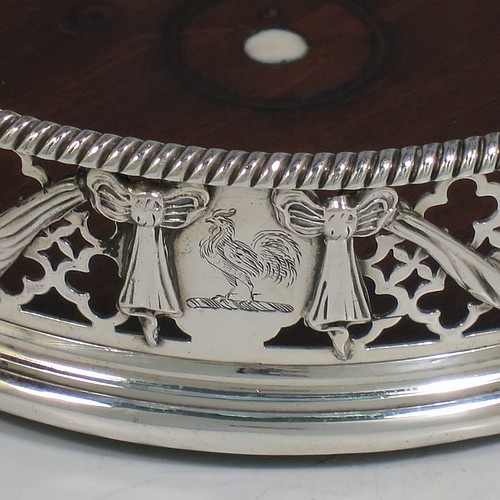 An Antique Georgian Neoclassical style Sterling Silver wine bottle table coaster, having a round hand-pierced body, with applied ribbons and swags on a hand-pierced body, together with an applied rope-twist or gadroon border, and a wood-turned base with bone button. Made by Elizabeth Jones of London in 1774. The dimensions of this fine hand-made antique silver wine bottle coaster are diameter 11 cms (4.3 inches), and height 3.5 cms (1.3 inches).