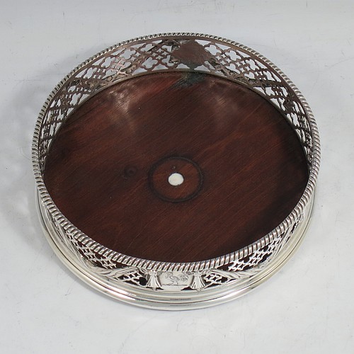 An Antique Georgian Neoclassical style Sterling Silver wine bottle table coaster, having a round hand-pierced body, with applied ribbons and swags on a hand-pierced body, together with an applied rope-twist or gadroon border, and a wood-turned base with bone button. Made by Elizabeth Jones of London in 1774. The dimensions of this fine hand-made antique silver wine bottle coaster are diameter 11 cms (4.3 inches), and height 3.5 cms (1.3 inches).
