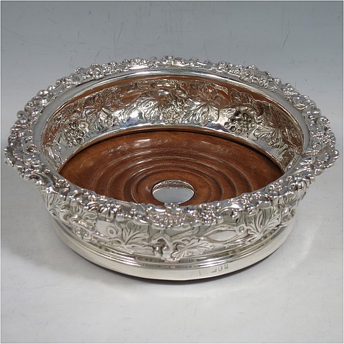 An Antique Georgian Sterling Silver pair of table wine bottle coasters, having round bellied bodies with hand-chased grape and vine decoration, and applied shell and scroll borders, and wood turned bases with silver buttons. Made S. C. Younge & Co of Sheffield in 1824. The dimensions of this fine pair of hand-made antique silver wine bottle coasters are diameter 16.5 cms (6.5 inches), and height 5 cms (2 inches).    