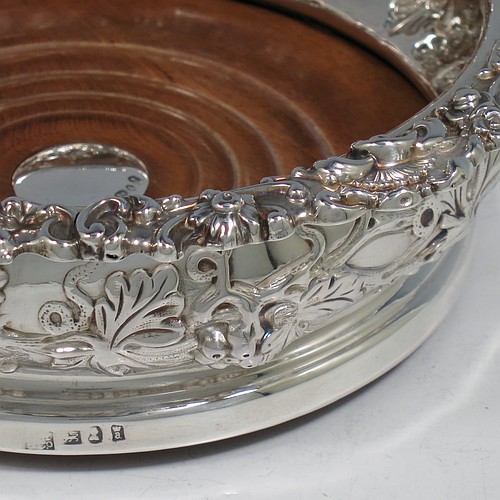 An Antique Georgian Sterling Silver pair of table wine bottle coasters, having round bellied bodies with hand-chased grape and vine decoration, and applied shell and scroll borders, and wood turned bases with silver buttons. Made S. C. Younge & Co of Sheffield in 1824. The dimensions of this fine pair of hand-made antique silver wine bottle coasters are diameter 16.5 cms (6.5 inches), and height 5 cms (2 inches).    