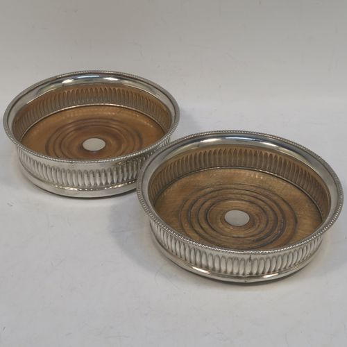 A very handsome Antique Georgian Old Sheffield plated pair of table wine coasters, in a Regency style, having round bellied bodies, with applied gadroon borders, and hand-chased fluted decoration, and with wood-turned bases and silver buttons. Made in ca. 1810. The dimensions of this fine pair of antique hand-made Old Sheffield plated wine bottle coasters are diameter 14 cms (5.5 inches), and height 4 cms (1.5 inches).   