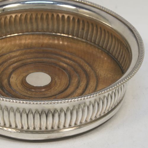 A very handsome Antique Georgian Old Sheffield plated pair of table wine coasters, in a Regency style, having round bellied bodies, with applied gadroon borders, and hand-chased fluted decoration, and with wood-turned bases and silver buttons. Made in ca. 1810. The dimensions of this fine pair of antique hand-made Old Sheffield plated wine bottle coasters are diameter 14 cms (5.5 inches), and height 4 cms (1.5 inches).