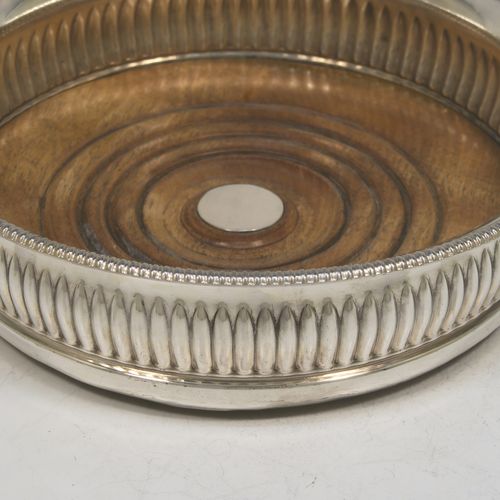 A very handsome Antique Georgian Old Sheffield plated pair of table wine coasters, in a Regency style, having round bellied bodies, with applied gadroon borders, and hand-chased fluted decoration, and with wood-turned bases and silver buttons. Made in ca. 1810. The dimensions of this fine pair of antique hand-made Old Sheffield plated wine bottle coasters are diameter 14 cms (5.5 inches), and height 4 cms (1.5 inches).