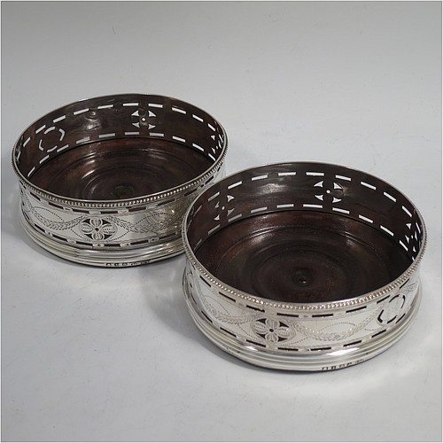 A very pretty Antique Georgian Sterling Silver pair of Neoclassical style wine coasters, having hand-pierced walls with hand-engraved neoclassical decoration, applied bead-edge borders, and oak hand-turned bases. Made by Benjamin Mountigue of London in 1786. The dimensions of this fine hand-made antique pair of neoclassical style silver wine bottle coasters are diameter 11.5 cms (4.5 inches), and height 4 cms (1.5 inches).