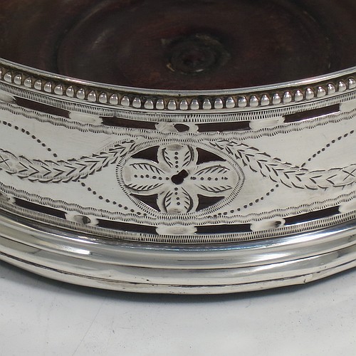 A very pretty Antique Georgian Sterling Silver pair of Neoclassical style wine coasters, having hand-pierced walls with hand-engraved neoclassical decoration, applied bead-edge borders, and oak hand-turned bases. Made by Benjamin Mountigue of London in 1786. The dimensions of this fine hand-made antique pair of neoclassical style silver wine bottle coasters are diameter 11.5 cms (4.5 inches), and height 4 cms (1.5 inches).