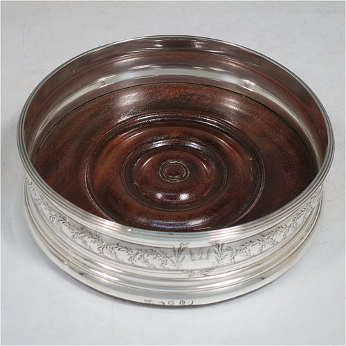 An Antique Georgian Sterling Silver very handsome and heavy set of four table wine bottle coasters, having round bellied bodies, with applied reed-edged borders and bands of hand-engraved floral decoration, and with wood-turned bases. Made by John Emes of London in 1800. The dimensions of these fine hand-made antique silver wine bottle coasters are diameter 13 cms (5 inches), and height 4 cms (1.5 inches). Please note that one of the coaster woods has been replaced at a later date and is of a slightly different colour.   