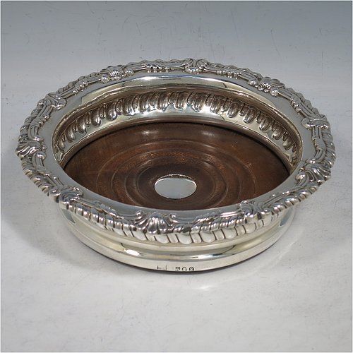 An Antique Georgian Sterling Silver pair of table wine bottle coasters, in a Regency style having round bodies with a band of hand-chased fluted decoration, applied gadroon, scroll, & shell borders, and wood turned bases with silver buttons. Made S. C. Younge & Co of Sheffield in 1815. The dimensions of this fine pair of hand-made antique silver wine bottle coasters are diameter 16 cms (6.3 inches), and height 4 cms (1.5 inches).