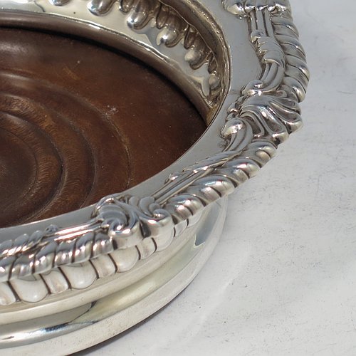 An Antique Georgian Sterling Silver pair of table wine bottle coasters, in a Regency style having round bodies with a band of hand-chased fluted decoration, applied gadroon, scroll, & shell borders, and wood turned bases with silver buttons. Made S. C. Younge & Co of Sheffield in 1815. The dimensions of this fine pair of hand-made antique silver wine bottle coasters are diameter 16 cms (6.3 inches), and height 4 cms (1.5 inches).
