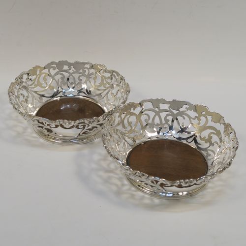 A very pretty pair of Antique early Victorian Sterling Silver wine bottle coasters, having hand-pierced sides with floral and scrol decoration, with applied cast floral borders, and original wood-turned bases. These beautiful antique silver wine bottle coasters were made by William Comyns of London in 1844. The dimensions of these fine hand-made antique silver wine coasters are diameter at top 14.5 cms (5.75 inches), diameter at base 10 cms (4 inches), and height 5 cms (2 inches).   