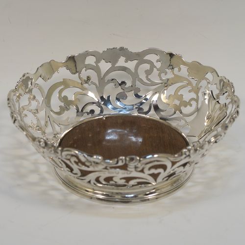 A very pretty pair of Antique early Victorian Sterling Silver wine bottle coasters, having hand-pierced sides with floral and scrol decoration, with applied cast floral borders, and original wood-turned bases. These beautiful antique silver wine bottle coasters were made by William Comyns of London in 1844. The dimensions of these fine hand-made antique silver wine coasters are diameter at top 14.5 cms (5.75 inches), diameter at base 10 cms (4 inches), and height 5 cms (2 inches).