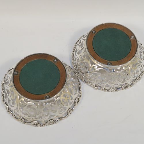 A very pretty pair of Antique early Victorian Sterling Silver wine bottle coasters, having hand-pierced sides with floral and scrol decoration, with applied cast floral borders, and original wood-turned bases. These beautiful antique silver wine bottle coasters were made by William Comyns of London in 1844. The dimensions of these fine hand-made antique silver wine coasters are diameter at top 14.5 cms (5.75 inches), diameter at base 10 cms (4 inches), and height 5 cms (2 inches).