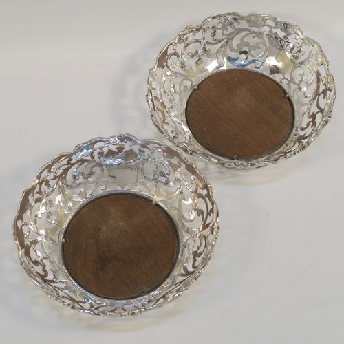 A very pretty pair of Antique early Victorian Sterling Silver wine bottle coasters, having hand-pierced sides with floral and scrol decoration, with applied cast floral borders, and original wood-turned bases. These beautiful antique silver wine bottle coasters were made by William Comyns of London in 1844. The dimensions of these fine hand-made antique silver wine coasters are diameter at top 14.5 cms (5.75 inches), diameter at base 10 cms (4 inches), and height 5 cms (2 inches).