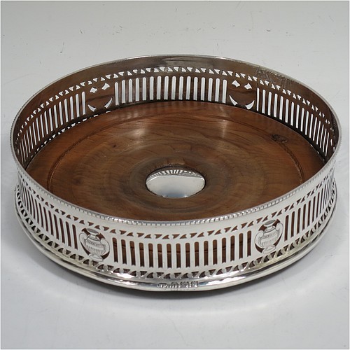 A very pretty Antique Neoclassical style Sterling Silver wine bottle table coaster, having a round hand-pierced body, with  an applied bead-edged border, and a wood-turned base with silver button. Made by Harry Freeman of London in 1915. The dimensions of this fine hand-made antique silver wine bottle coaster are diameter 14.5 cms (5.75 inches), and height 4 cms (1.5 inches).    