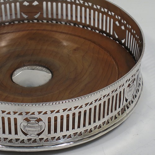 A very pretty Antique Neoclassical style Sterling Silver wine bottle table coaster, having a round hand-pierced body, with an applied bead-edged border, and a wood-turned base with silver button. Made by Harry Freeman of London in 1915. The dimensions of this fine hand-made antique silver wine bottle coaster are diameter 14.5 cms (5.75 inches), and height 4 cms (1.5 inches).