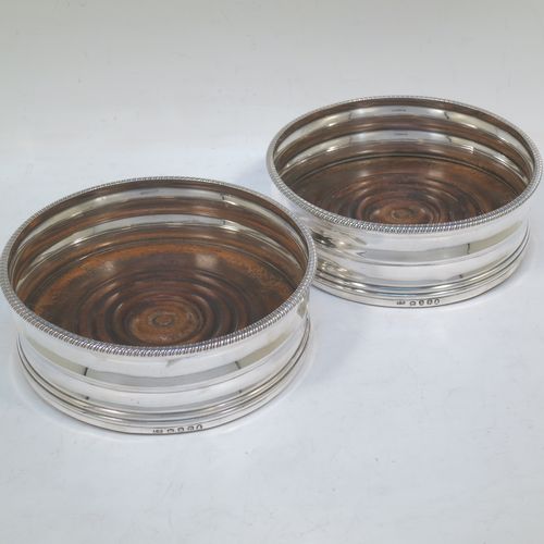A very elegant pair of Antique Georgian Sterling Silver table wine bottle coasters, having plain round double bellied bodies, with applied gadroon or rope-twist borders, and oak wood turned bases. Made by James Barratt of London in 1812. The dimensions of these fine hand-made antique silver wine bottle coasters are diameter 13 cms (3.25 inches), and height 5 cms (2 inches).   