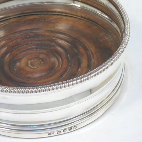 A very elegant pair of Antique Georgian Sterling Silver table wine bottle coasters, having plain round double bellied bodies, with applied gadroon or rope-twist borders, and oak wood turned bases. Made by James Barratt of London in 1812. The dimensions of these fine hand-made antique silver wine bottle coasters are diameter 13 cms (3.25 inches), and height 5 cms (2 inches).   