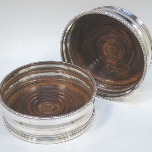 A very elegant pair of Antique Georgian Sterling Silver table wine bottle coasters, having plain round double bellied bodies, with applied gadroon or rope-twist borders, and oak wood turned bases. Made by James Barratt of London in 1812. The dimensions of these fine hand-made antique silver wine bottle coasters are diameter 13 cms (3.25 inches), and height 5 cms (2 inches).   