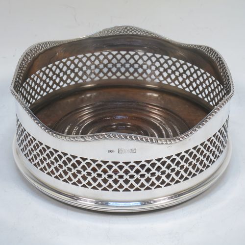 A very pretty Neoclassical style Sterling Silver wine bottle table coaster, having a round hand-pierced body, with an applied gadroon border, and a wood-turned base. Made by S. J. Rose of Birmingham in 1973. The dimensions of this fine hand-made silver wine bottle coaster are diameter 13.5 cms (5.3 inches), and height 5.5 cms (2.25 inches).   