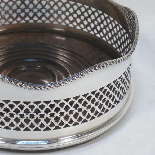 A very pretty Neoclassical style Sterling Silver wine bottle table coaster, having a round hand-pierced body, with an applied gadroon border, and a wood-turned base. Made by S. J. Rose of Birmingham in 1973. The dimensions of this fine hand-made silver wine bottle coaster are diameter 13.5 cms (5.3 inches), and height 5.5 cms (2.25 inches).