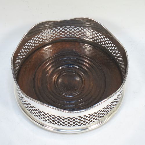 A very pretty Neoclassical style Sterling Silver wine bottle table coaster, having a round hand-pierced body, with an applied gadroon border, and a wood-turned base. Made by S. J. Rose of Birmingham in 1973. The dimensions of this fine hand-made silver wine bottle coaster are diameter 13.5 cms (5.3 inches), and height 5.5 cms (2.25 inches).