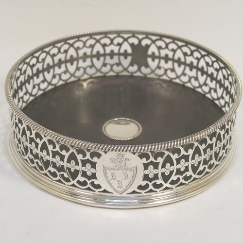 A beautiful and large Antique Georgian Neoclassical style Sterling Silver wine bottle table coaster, having a round hand-pierced body with floral and scroll decoration, together with an applied rope-twist or gadroon border, and a wood-turned base with silver button. This elegant antique silver wine bottle coaster was made by Edward Lowe of London in 1775. The dimensions of this fine hand-made antique silver wine bottle coaster are diameter 14.5 cms (5.75 inches), and height 4.5 cms (1.75 inches). Please note that this item is crested.  