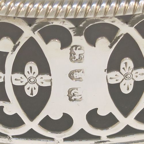 A beautiful and large Antique Georgian Neoclassical style Sterling Silver wine bottle table coaster, having a round hand-pierced body with floral and scroll decoration, together with an applied rope-twist or gadroon border, and a wood-turned base with silver button. This elegant antique silver wine bottle coaster was made by Edward Lowe of London in 1775. The dimensions of this fine hand-made antique silver wine bottle coaster are diameter 14.5 cms (5.75 inches), and height 4.5 cms (1.75 inches). Please note that this item is crested.  