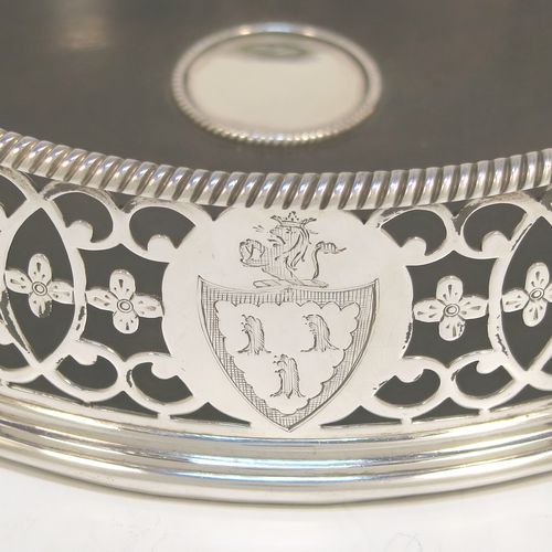 A beautiful and large Antique Georgian Neoclassical style Sterling Silver wine bottle table coaster, having a round hand-pierced body with floral and scroll decoration, together with an applied rope-twist or gadroon border, and a wood-turned base with silver button. This elegant antique silver wine bottle coaster was made by Edward Lowe of London in 1775. The dimensions of this fine hand-made antique silver wine bottle coaster are diameter 14.5 cms (5.75 inches), and height 4.5 cms (1.75 inches). Please note that this item is crested.  