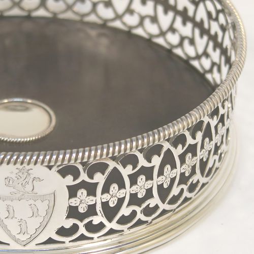 A beautiful and large Antique Georgian Neoclassical style Sterling Silver wine bottle table coaster, having a round hand-pierced body with floral and scroll decoration, together with an applied rope-twist or gadroon border, and a wood-turned base with silver button. This elegant antique silver wine bottle coaster was made by Edward Lowe of London in 1775. The dimensions of this fine hand-made antique silver wine bottle coaster are diameter 14.5 cms (5.75 inches), and height 4.5 cms (1.75 inches). Please note that this item is crested.  