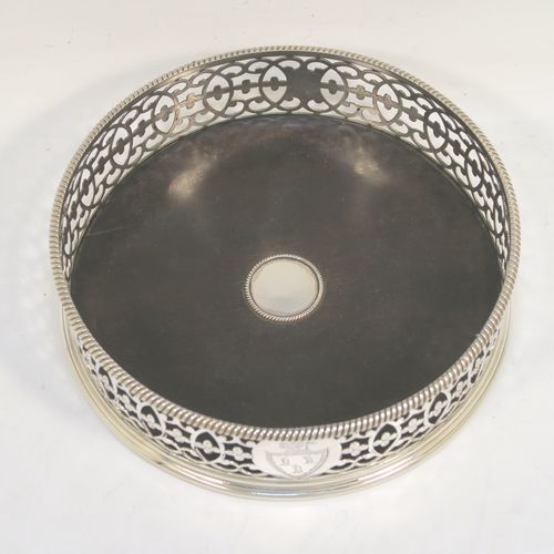 A beautiful and large Antique Georgian Neoclassical style Sterling Silver wine bottle table coaster, having a round hand-pierced body with floral and scroll decoration, together with an applied rope-twist or gadroon border, and a wood-turned base with silver button. This elegant antique silver wine bottle coaster was made by Edward Lowe of London in 1775. The dimensions of this fine hand-made antique silver wine bottle coaster are diameter 14.5 cms (5.75 inches), and height 4.5 cms (1.75 inches). Please note that this item is crested.  