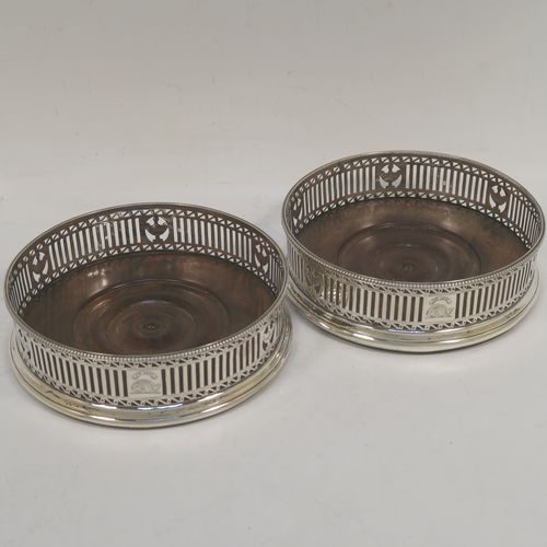 A very handsome Antique Georgian Sterling Silver pair of Neoclassical style wine coasters, having hand-pierced walls, applied bead-edged borders, and plain oak-turned bases. These beautiful antique silver bottle coasters were made by Robert Hennell of London in 1780. The dimensions of this fine hand-made antique pair of silver wine bottle coasters are diameter 12 cms (4.75 inches), and height 3.5 cms (1.3 inches). Please note that these items are crested.