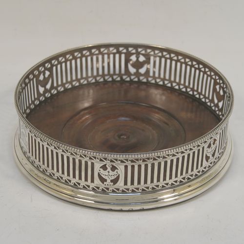 A very handsome Antique Georgian Sterling Silver pair of Neoclassical style wine coasters, having hand-pierced walls, applied bead-edged borders, and plain oak-turned bases. These beautiful antique silver bottle coasters were made by Robert Hennell of London in 1780. The dimensions of this fine hand-made antique pair of silver wine bottle coasters are diameter 12 cms (4.75 inches), and height 3.5 cms (1.3 inches). Please note that these items are crested.
