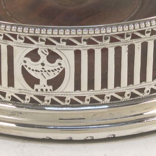 A very handsome Antique Georgian Sterling Silver pair of Neoclassical style wine coasters, having hand-pierced walls, applied bead-edged borders, and plain oak-turned bases. These beautiful antique silver bottle coasters were made by Robert Hennell of London in 1780. The dimensions of this fine hand-made antique pair of silver wine bottle coasters are diameter 12 cms (4.75 inches), and height 3.5 cms (1.3 inches). Please note that these items are crested.