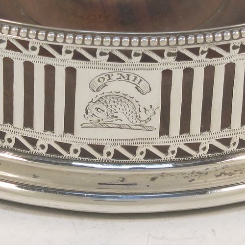 A very handsome Antique Georgian Sterling Silver pair of Neoclassical style wine coasters, having hand-pierced walls, applied bead-edged borders, and plain oak-turned bases. These beautiful antique silver bottle coasters were made by Robert Hennell of London in 1780. The dimensions of this fine hand-made antique pair of silver wine bottle coasters are diameter 12 cms (4.75 inches), and height 3.5 cms (1.3 inches). Please note that these items are crested.
