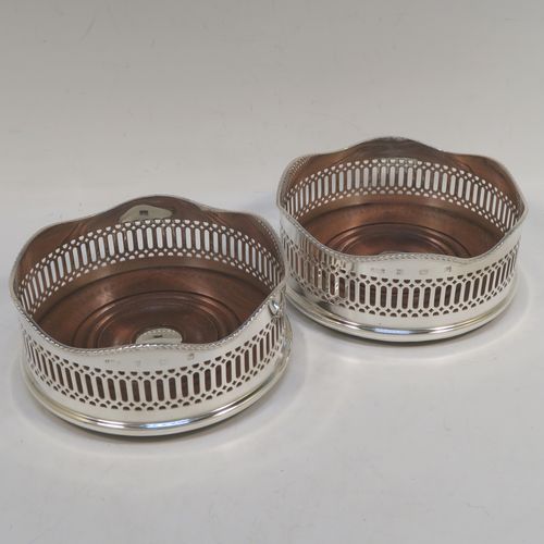 A large and very elegant Sterling Silver pair of Neoclassical style wine coasters, having hand-pierced walls with  applied wavy gadroon-edged borders, and plain oak-turned bases with silver buttons. These beautiful silver bottle coasters were made by R. E. Porter of Birmingham in 1989. The dimensions of this fine hand-made pair of silver wine bottle coasters are diameter 14 cms (5.5 inches), and height 5.5 cms (2.25 inches).   
