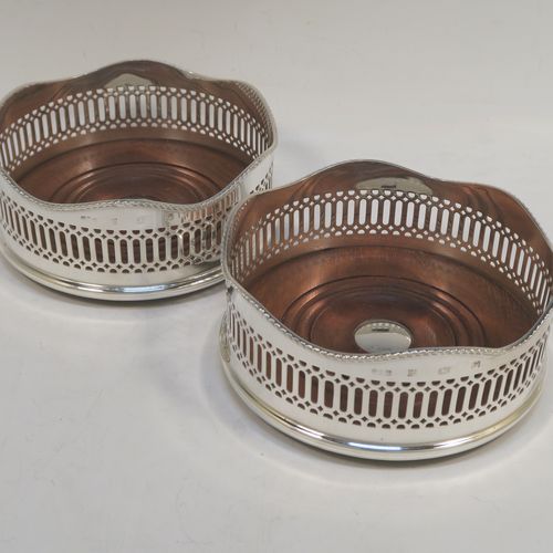 A large and very elegant Sterling Silver pair of Neoclassical style wine coasters, having hand-pierced walls with applied wavy gadroon-edged borders, and plain oak-turned bases with silver buttons. These beautiful silver bottle coasters were made by R. E. Porter of Birmingham in 1989. The dimensions of this fine hand-made pair of silver wine bottle coasters are diameter 14 cms (5.5 inches), and height 5.5 cms (2.25 inches).