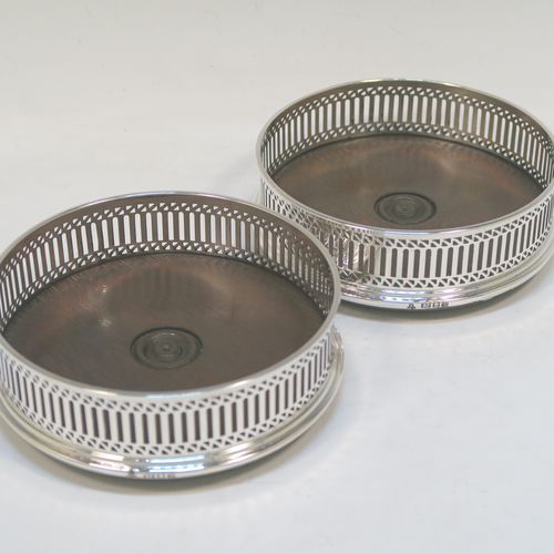 A very elegant Sterling Silver pair of Neoclassical style wine coasters, having hand-pierced walls with   plain oak turned bases. These beautiful silver bottle coasters were made by M. C. Hersey of London  in 1986. The dimensions of this fine hand-made pair of silver wine bottle coasters are diameter 12.5 cms (5 inches), and height 4 cms (1.5 inches).   