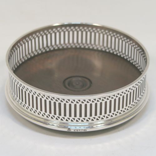 A very elegant Sterling Silver pair of Neoclassical style wine coasters, having hand-pierced walls with plain oak turned bases. These beautiful silver bottle coasters were made by M. C. Hersey of London in 1986. The dimensions of this fine hand-made pair of silver wine bottle coasters are diameter 12.5 cms (5 inches), and height 4 cms (1.5 inches).