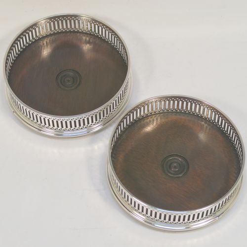 A very elegant Sterling Silver pair of Neoclassical style wine coasters, having hand-pierced walls with plain oak turned bases. These beautiful silver bottle coasters were made by M. C. Hersey of London in 1986. The dimensions of this fine hand-made pair of silver wine bottle coasters are diameter 12.5 cms (5 inches), and height 4 cms (1.5 inches).