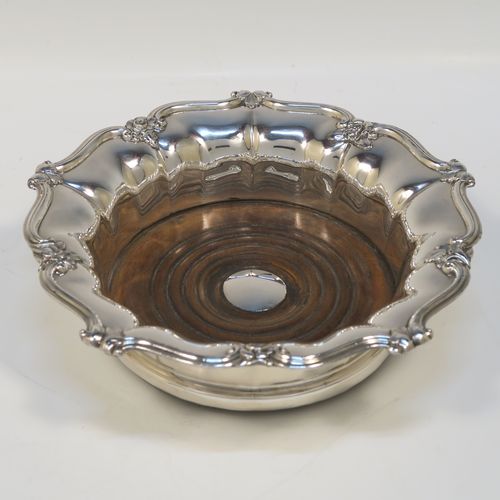 A very handsome Antique Georgian Old Sheffield plated pair of table wine coasters, having round bodies with melon fluted sides, applied floral and scroll borders, and wood-turned bases with silver buttons. These elegant antique wine bottle coasters were made in ca. 1830. The dimensions of this fine hand-made pair of antique Old Sheffield silver plated wine coasters are diameter 18 cms (7 inches), and height 5 cms (2 inches).