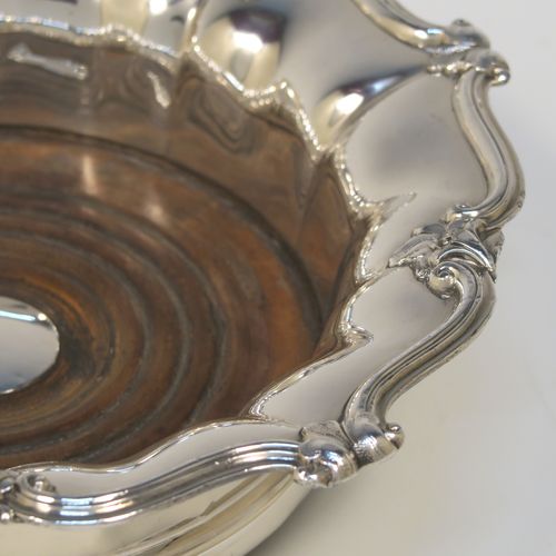 A very handsome Antique Georgian Old Sheffield plated pair of table wine coasters, having round bodies with melon fluted sides, applied floral and scroll borders, and wood-turned bases with silver buttons. These elegant antique wine bottle coasters were made in ca. 1830. The dimensions of this fine hand-made pair of antique Old Sheffield silver plated wine coasters are diameter 18 cms (7 inches), and height 5 cms (2 inches).