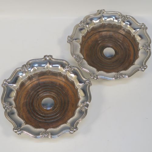 A very handsome Antique Georgian Old Sheffield plated pair of table wine coasters, having round bodies with melon fluted sides, applied floral and scroll borders, and wood-turned bases with silver buttons. These elegant antique wine bottle coasters were made in ca. 1830. The dimensions of this fine hand-made pair of antique Old Sheffield silver plated wine coasters are diameter 18 cms (7 inches), and height 5 cms (2 inches).