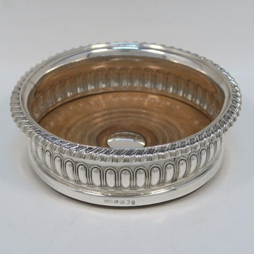 A very handsome Antique Georgian Sterling Silver wine bottle table coaster, in a Regency style, having a round bellied body with a hand-chased melon  vertical fluting, an applied gadroon border, and an oak wood-turned base with central silver button. This elegant silver bottle coaster was made by Thomas and John Settle of London in 1819. The dimensions of this fine hand-made antique silver wine bottle coaster are diameter 15 cms (6 inches), and height 5 cms (2 inches).   