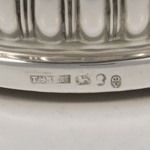 A very handsome Antique Georgian Sterling Silver wine bottle table coaster, in a Regency style, having a round bellied body with a hand-chased melon vertical fluting, an applied gadroon border, and an oak wood-turned base with central silver button. This elegant silver bottle coaster was made by Thomas and John Settle of London in 1819. The dimensions of this fine hand-made antique silver wine bottle coaster are diameter 15 cms (6 inches), and height 5 cms (2 inches).