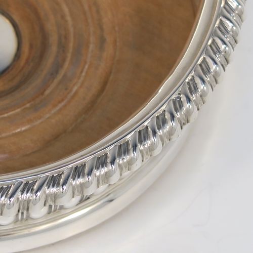 A very handsome Antique Georgian Sterling Silver wine bottle table coaster, in a Regency style, having a round bellied body with a hand-chased melon vertical fluting, an applied gadroon border, and an oak wood-turned base with central silver button. This elegant silver bottle coaster was made by Thomas and John Settle of London in 1819. The dimensions of this fine hand-made antique silver wine bottle coaster are diameter 15 cms (6 inches), and height 5 cms (2 inches).
