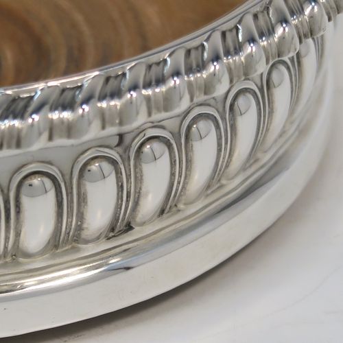 A very handsome Antique Georgian Sterling Silver wine bottle table coaster, in a Regency style, having a round bellied body with a hand-chased melon vertical fluting, an applied gadroon border, and an oak wood-turned base with central silver button. This elegant silver bottle coaster was made by Thomas and John Settle of London in 1819. The dimensions of this fine hand-made antique silver wine bottle coaster are diameter 15 cms (6 inches), and height 5 cms (2 inches).