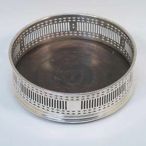 A very handsome Antique Georgian Old Sheffield Plated pair of Neoclassical style wine coasters, having hand-pierced walls, applied bead-edged borders, and plain oak-turned bases. These beautiful antique silver-plated bottle coasters were made in ca. 1780. The dimensions of this fine hand-made antique pair of Old Sheffield Plated silver wine bottle coasters are diameter 13 cms (5.25 inches), and height 4.5 cms (1.75 inches).