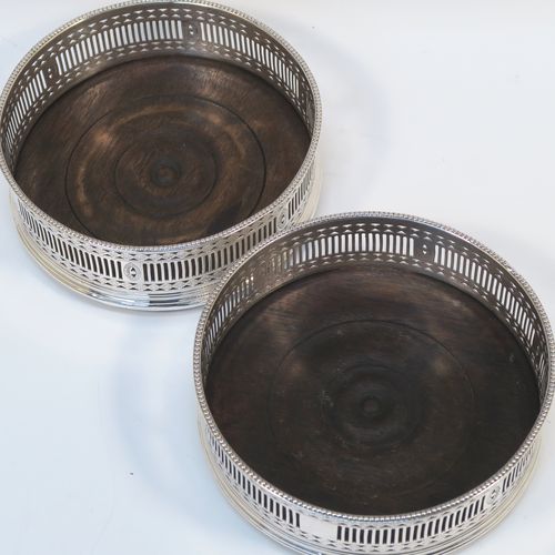 A very handsome Antique Georgian Old Sheffield Plated pair of Neoclassical style wine coasters, having hand-pierced walls, applied bead-edged borders, and plain oak-turned bases. These beautiful antique silver-plated bottle coasters were made in ca. 1780. The dimensions of this fine hand-made antique pair of Old Sheffield Plated silver wine bottle coasters are diameter 13 cms (5.25 inches), and height 4.5 cms (1.75 inches).