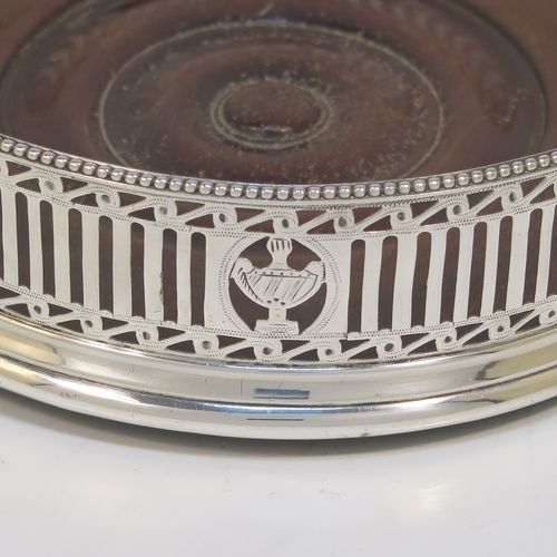 A very pretty Antique Georgian Neoclassical style Sterling Silver wine bottle table coaster, having a round hand-pierced body with geometrical and tureen style decoration, together with an applied bead-edged top border, and an wood-turned base. This beautiful antique silver wine bottle coaster was made in London in 1786. The dimensions of this fine hand-made antique silver wine bottle coaster are diameter 12 cms (4.75 inches), and height 3.5 cms (1.3 inches).