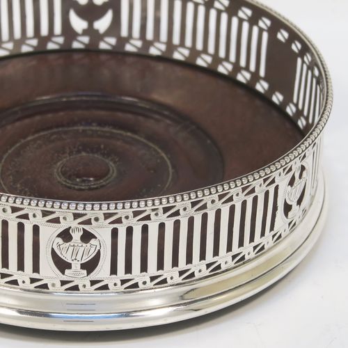 A very pretty Antique Georgian Neoclassical style Sterling Silver wine bottle table coaster, having a round hand-pierced body with geometrical and tureen style decoration, together with an applied bead-edged top border, and an wood-turned base. This beautiful antique silver wine bottle coaster was made in London in 1786. The dimensions of this fine hand-made antique silver wine bottle coaster are diameter 12 cms (4.75 inches), and height 3.5 cms (1.3 inches).